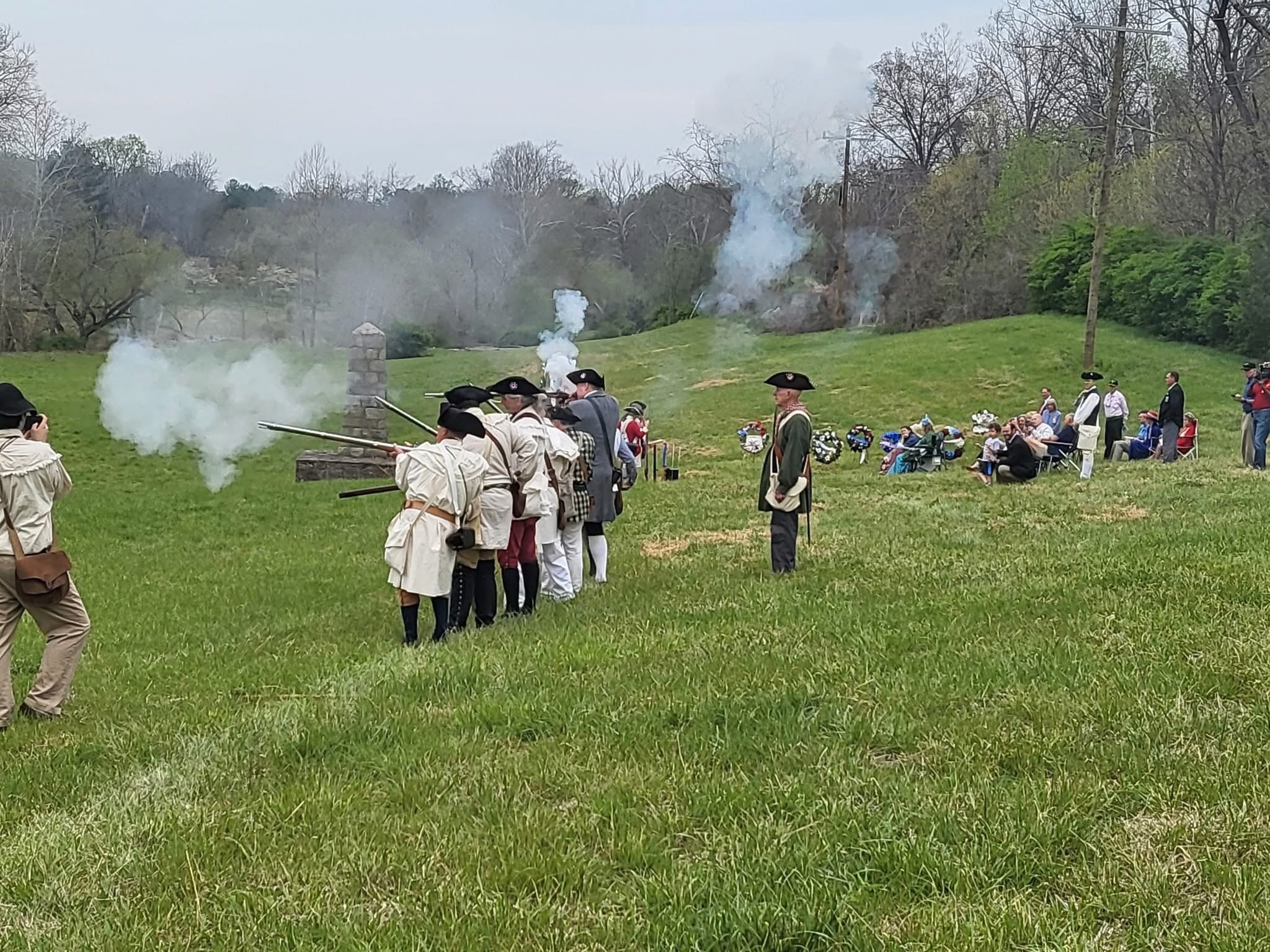 Reenactors dressed as militiamen fire shots in a musket volley on Champe Farms, depicting the initial battle at Lexington, Massachusetts.